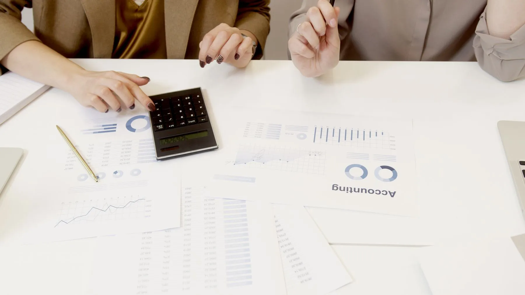 Duas pessoas analisam relatórios contábeis com uma calculadora sobre a mesa